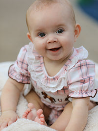 Smiling baby girl wearing pink plaid romper with white ruffled collar and Western horse embroidery on smocked bodice.