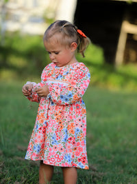Little girl in a floral Fall Pumpkin Bow Smock Dress with embroidered pumpkin bows outdoors.