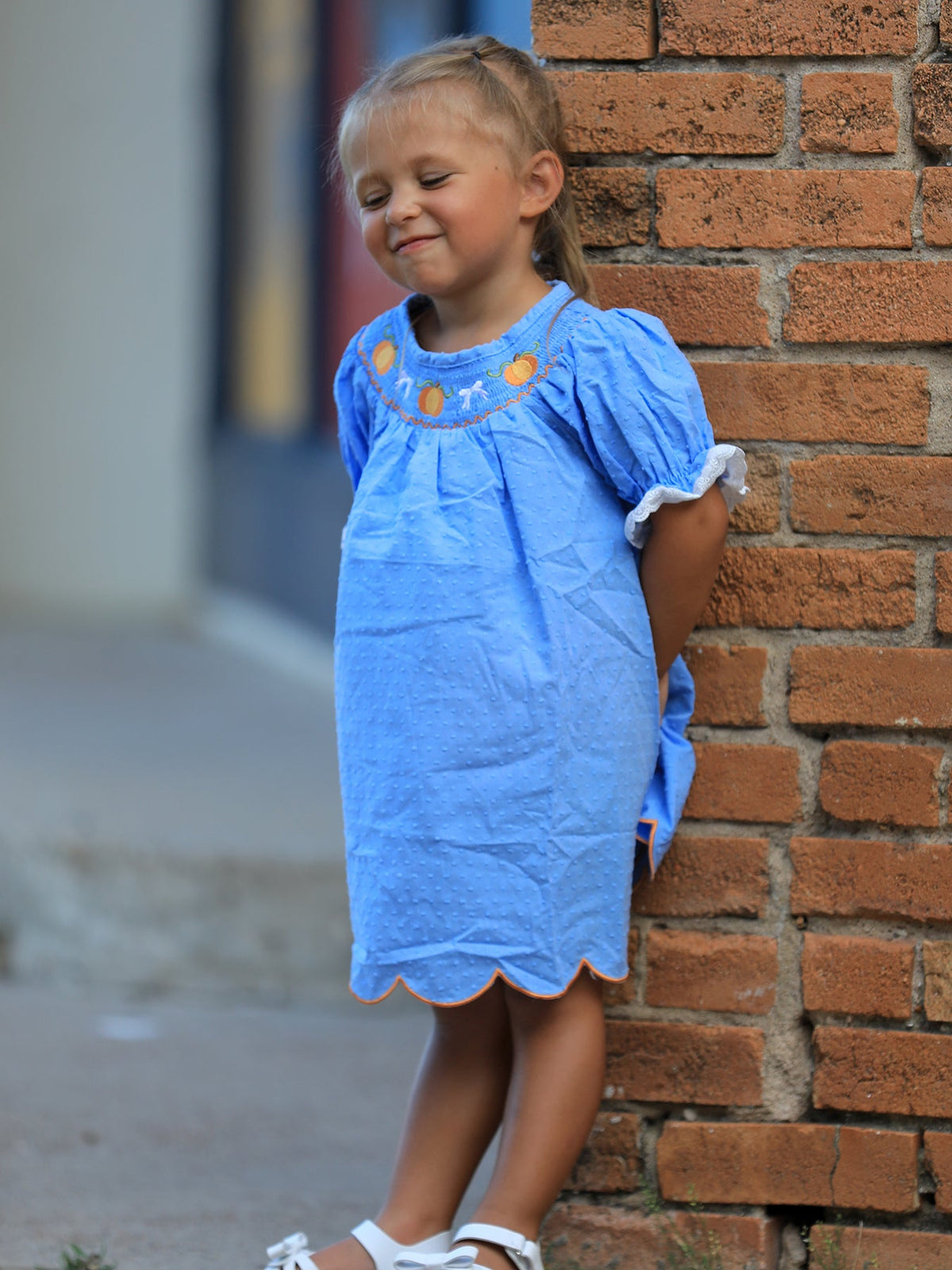 Blue baby girl dress with pumpkin embroidery, lace smock and scalloped orange hem for Thanksgiving and Halloween.