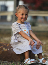 Little girl in plaid smock dress with pumpkin embroidery, ready for fall, Halloween, and Thanksgiving celebrations.