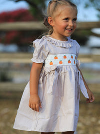Girl wearing plaid Fall Thanksgiving dress with pumpkin embroidery on a smocked panel.