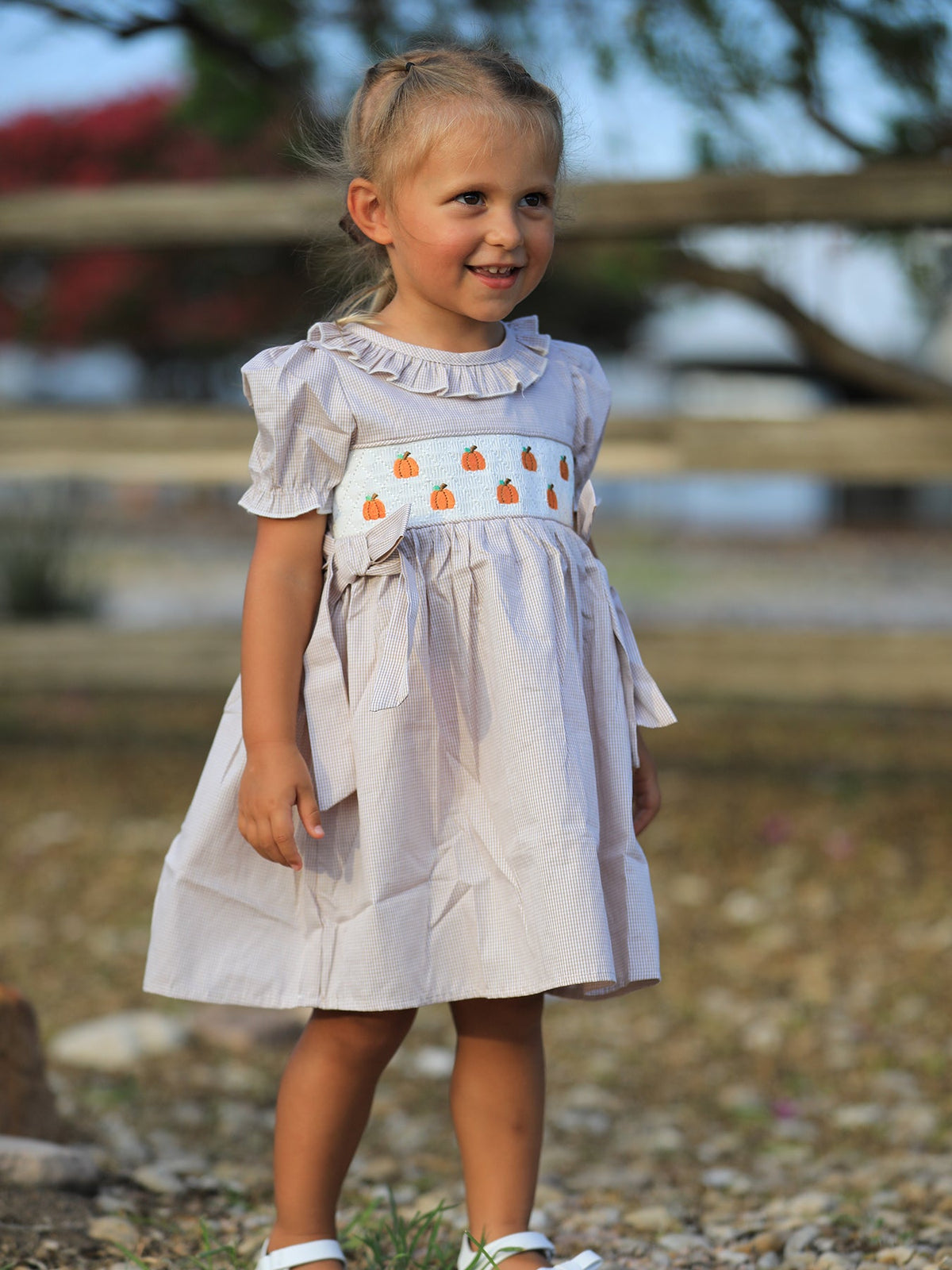 Fall pumpkin-embroidered plaid smock dress for girls, worn by a smiling little girl outdoors.