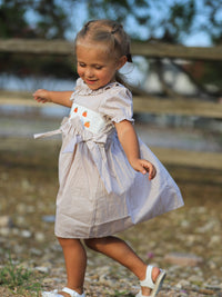 Little girl in fall plaid smock dress with pumpkin embroidery outdoors.