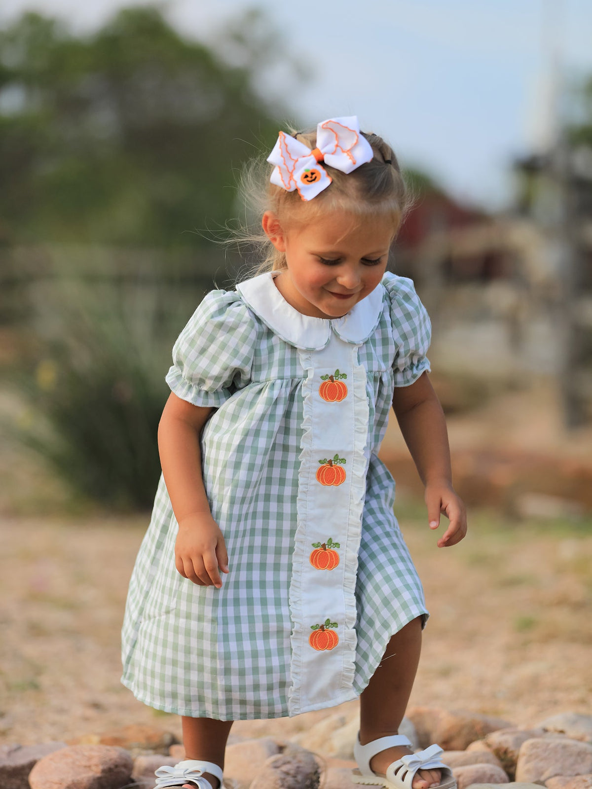 Girl in green plaid dress with pumpkin appliques and white collar, festive Fall/Halloween look.