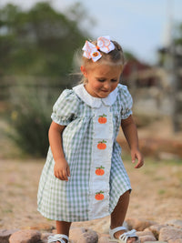 Girl in green plaid dress with pumpkin appliques and white collar, festive Fall/Halloween look.