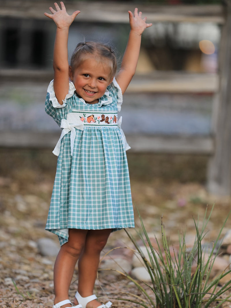 Happy girl in a mint plaid dress with puff sleeves, lace trim, and horse and cowboy boot embroidery.