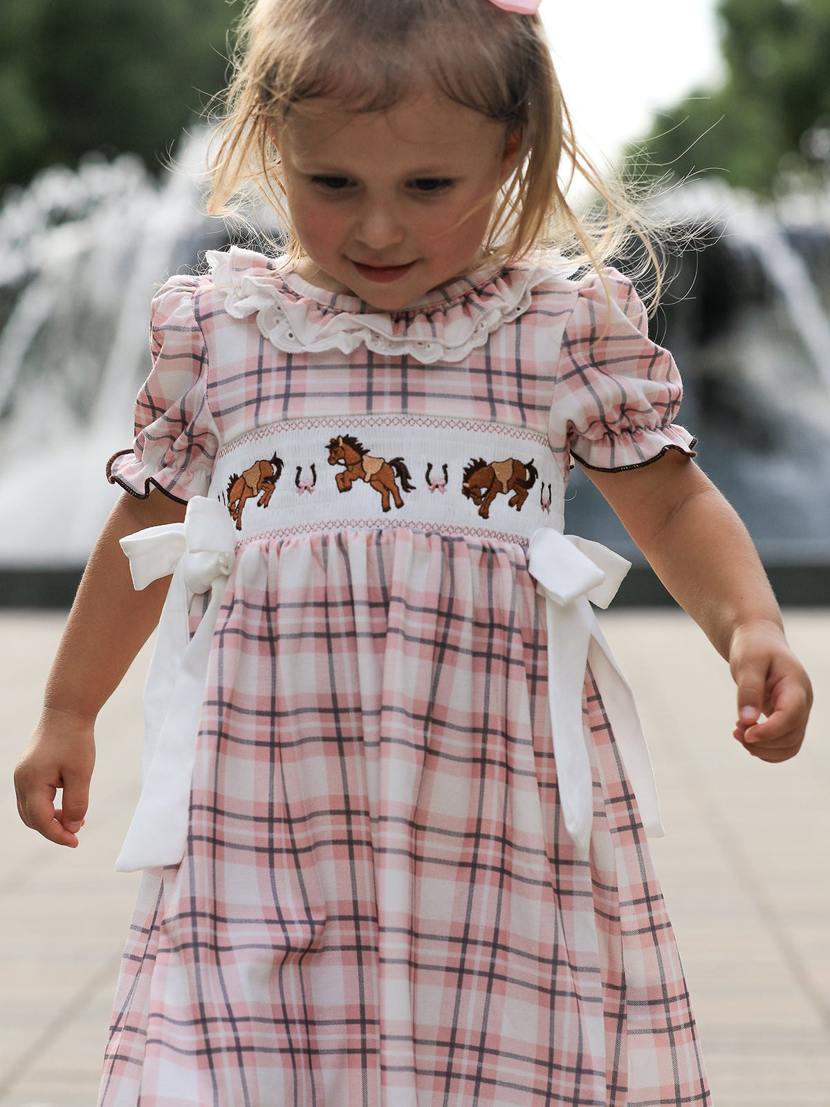 Pink plaid girls dress with horse embroidery, smocked bodice, ruffled collar, and white side bows.