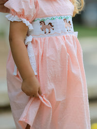 Pink girls dress with horse embroidery on smocked bodice, puff sleeves, lace trim, and textured fabric.