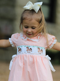 Pink girls dress with Western horse embroidery on smocked bodice, lace petals collar, puff sleeves, and white hair bow.