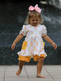 Young girl in a white dress with pink bows, yellow pockets, orange ruffled hem, and pink bow headband.