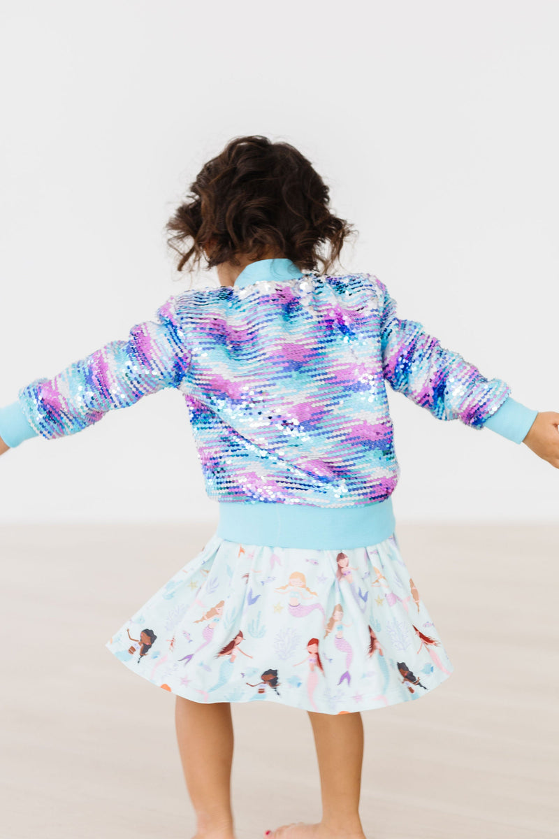 Back view of a girl wearing the vibrant Mermaid Sequin Jacket, highlighting its eye-catching design paired with a cute skirt.