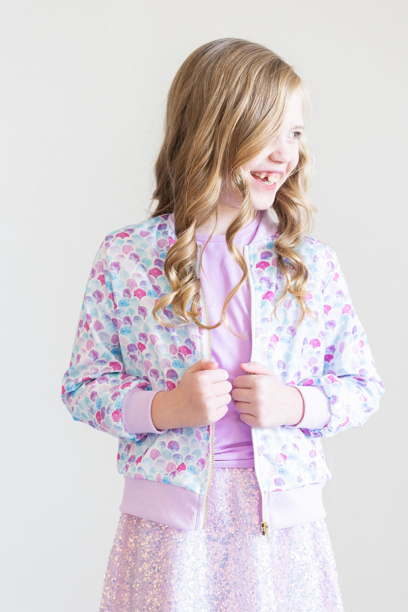 A smiling young girl happily poses in the Mermaid Scales Satin Jacket, highlighting its playful design paired with a sparkling skirt.
