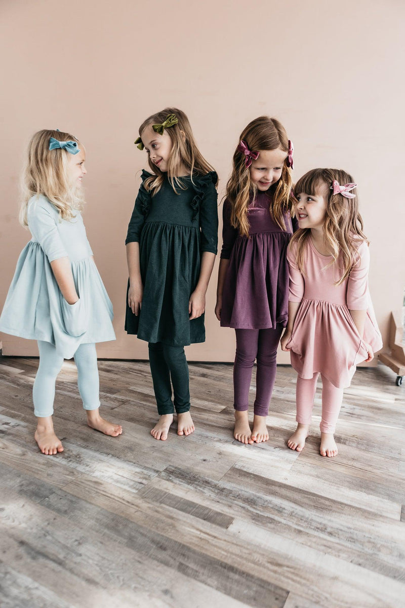 Four young girls wearing colorful dresses and leggings, including Vintage Pink Leggings from Mila & Rose, playfully interacting in a bright, stylish setting.