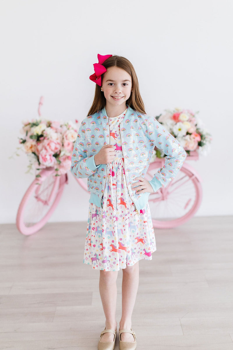 Charming young model wearing the Mint Rainbow Sequin Jacket over a dress, striking a pose with a pink bow in her hair, ready to shine bright.