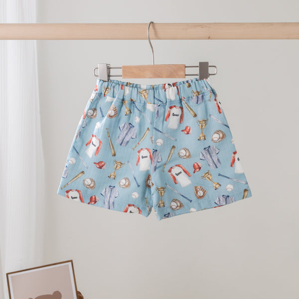 Blue shorts with cartoon character pattern hanging on a wooden rod against a white wall.