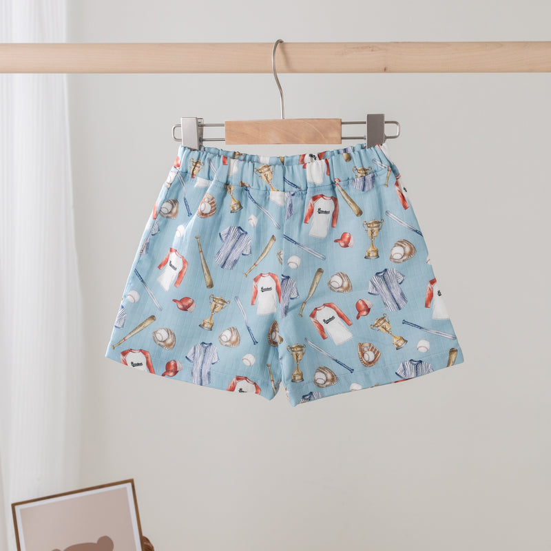 Blue shorts with cartoon character pattern hanging on a wooden rod against a white wall.