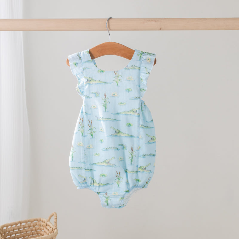 Gator Games Organic Muslin Bubble Romper on hanger, light blue with alligators and lily pads print.