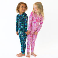 Two kids wearing The Second-Skin 2-Piece Long Sleeve Pajama in blue and pink, smiling.