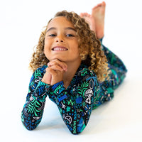 Child with curly hair wearing blue Mystic Mama Second-Skin 2-Piece Long Sleeve Pajama set, smiling.