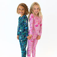 Two kids wearing Second-Skin 2-Piece Long Sleeve Pajamas in blue and pink, standing side by side.