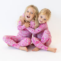 Two children in pink Mystic Mama Second-Skin 2-piece long-sleeve pajamas, smiling and hugging.
