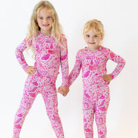 Two girls in pink Mystic Mama 2-piece long-sleeve pajamas with You Made Magic pattern.