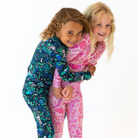 Two kids wearing Mystic Mama Second-Skin 2-Piece Long Sleeve Pajama sets in pink and blue, smiling and hugging.