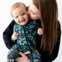 Mother with long brown hair kisses a smiling baby wearing a blue patterned zippered footie.
