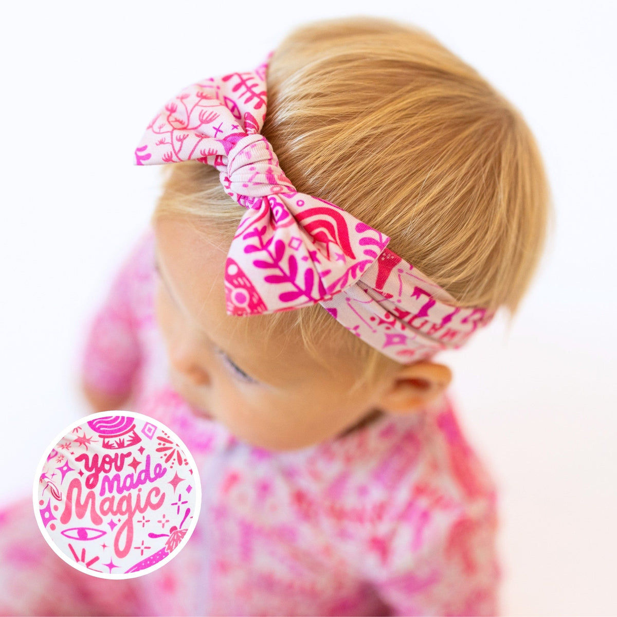 The SoftKnot Bow in pink on a baby head-wrap in CozyMa bamboo fabric with a joyful print.