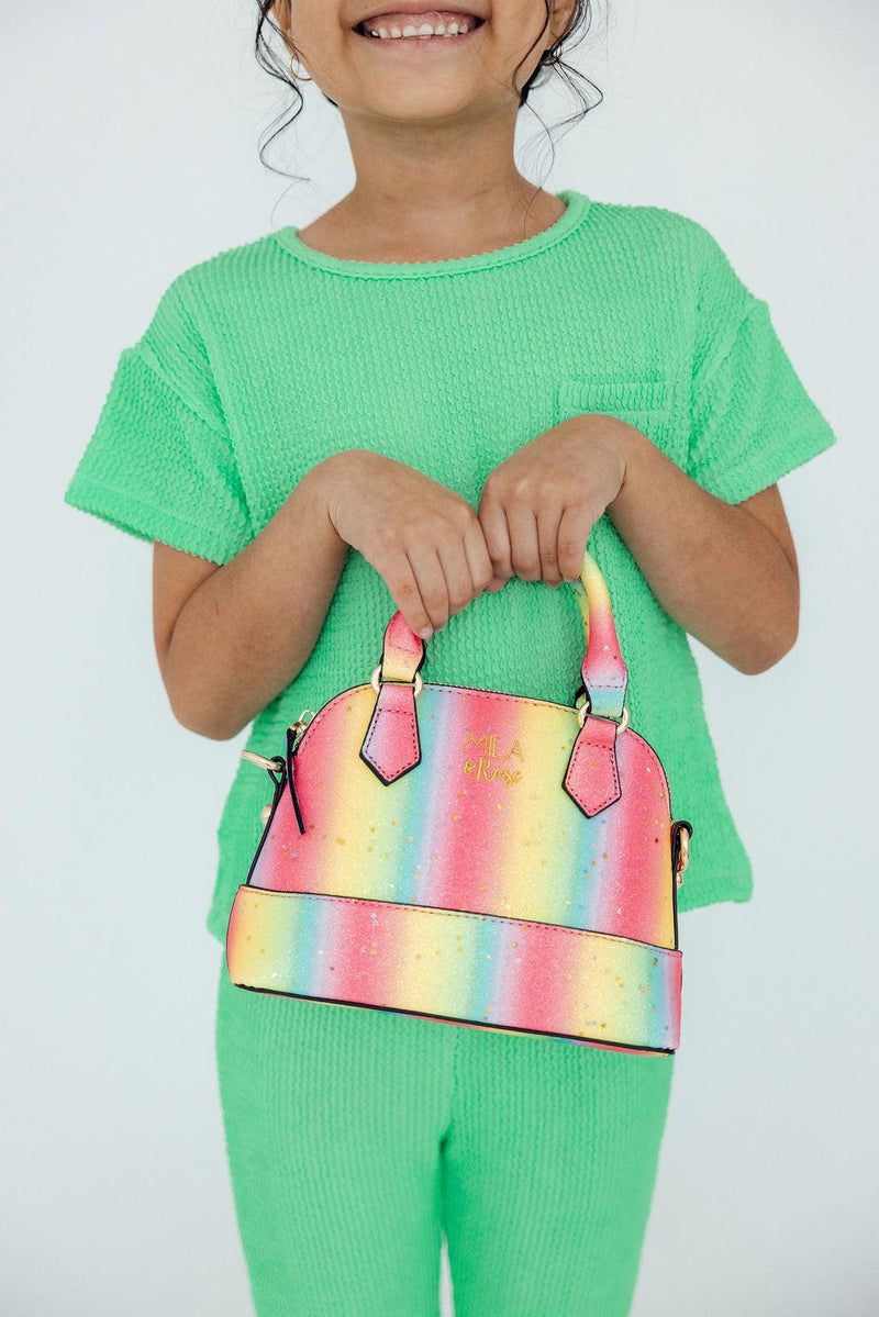 Girl holding a neon rainbow glitter crossbody purse with gold hardware and a top handle.