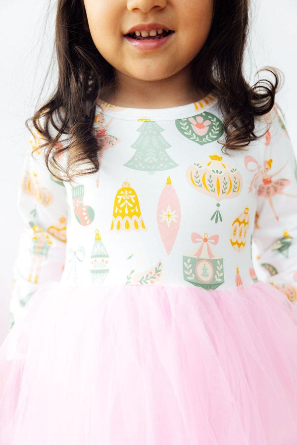 Girl wearing a long sleeve nutcracker tutu dress with holiday ornaments and a pink tulle skirt. Perfect for play or special occasions.
