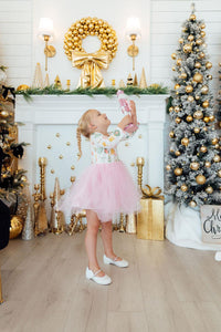 Toddler girl in a nutcracker long sleeve tutu dress with pink skirt holding a toy near a gold Christmas fireplace.
