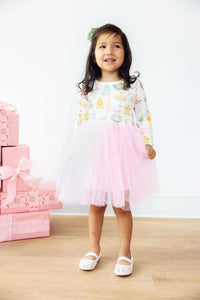 Girl in festive long sleeve tutu dress with holiday print and pink skirt, standing near stacked pink gifts. Perfect for dress up or special occasions.
