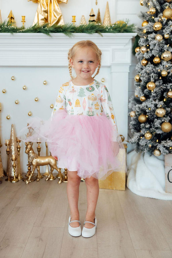 Girl wearing Nutcracker long sleeve tutu dress with pink skirt and holiday print, standing near Christmas tree.