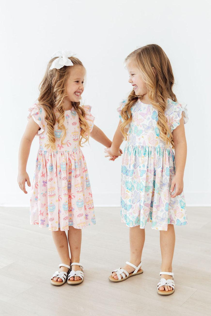 Two girls wear Off to the Circus Flutter Sleeve Twirl Dress in pastel prints with flutter sleeves and twirl skirts.