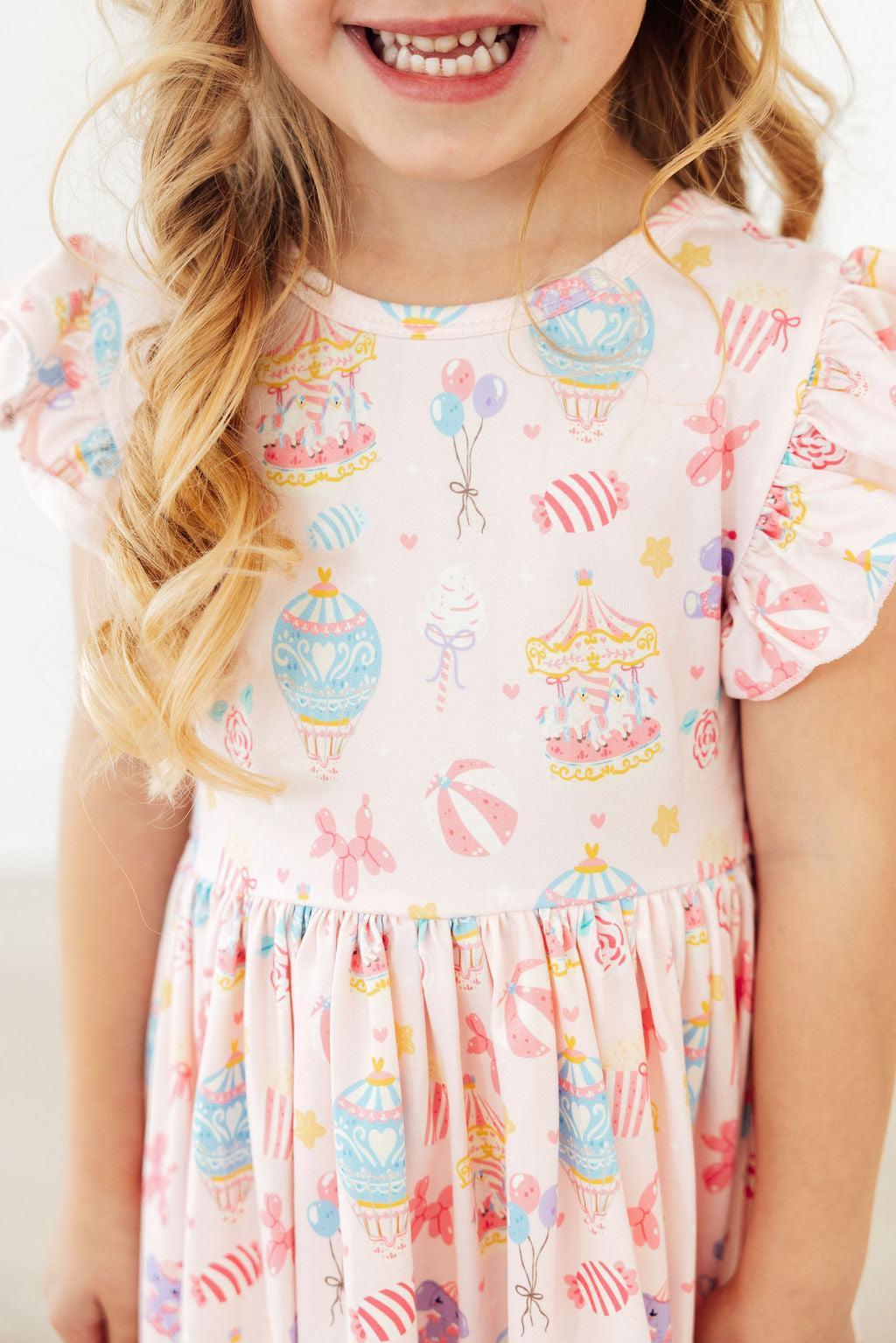 Off to the Circus Flutter Sleeve Twirl Dress worn by a smiling toddler, featuring circus print and twirl-ready style.