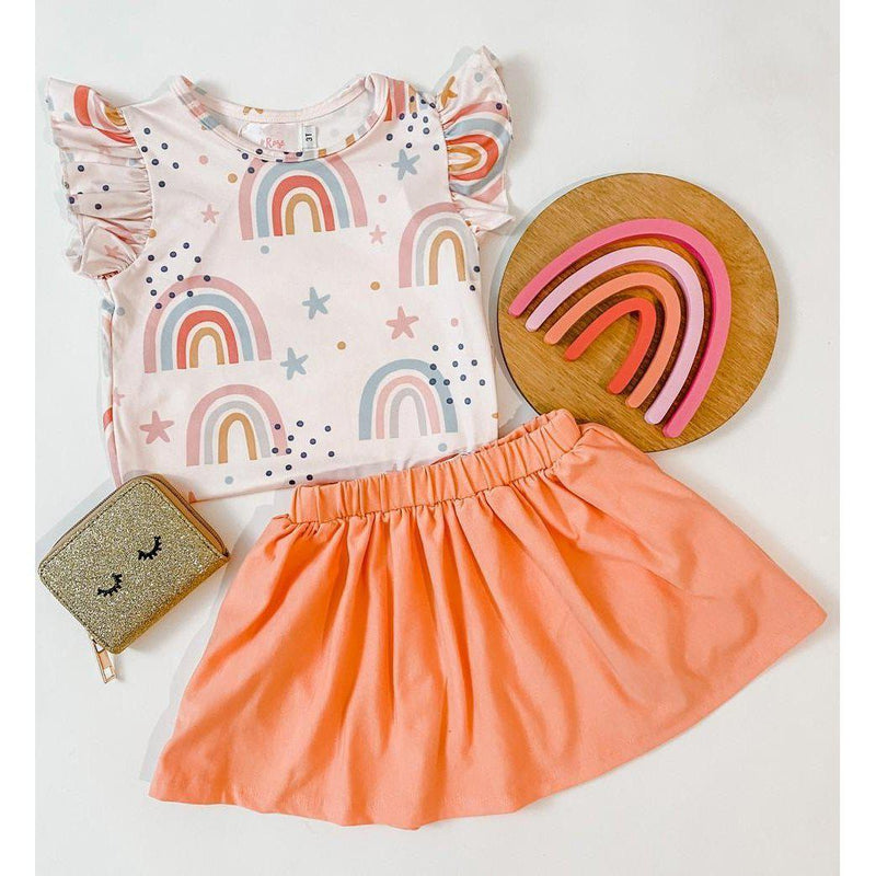 Over the Rainbow S/S Ruffle Tee paired with a peach skirt, rainbow-themed accessories, and playful atmosphere, perfect for little girls who love to twirl and shine.