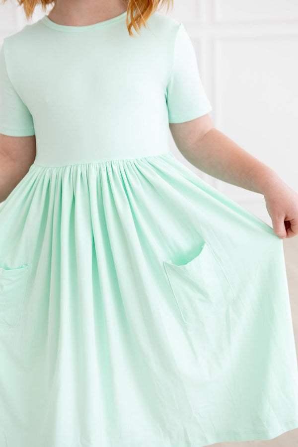 Pastel green short-sleeve pocket twirl dress for girls with gathered waist and pockets on the skirt.