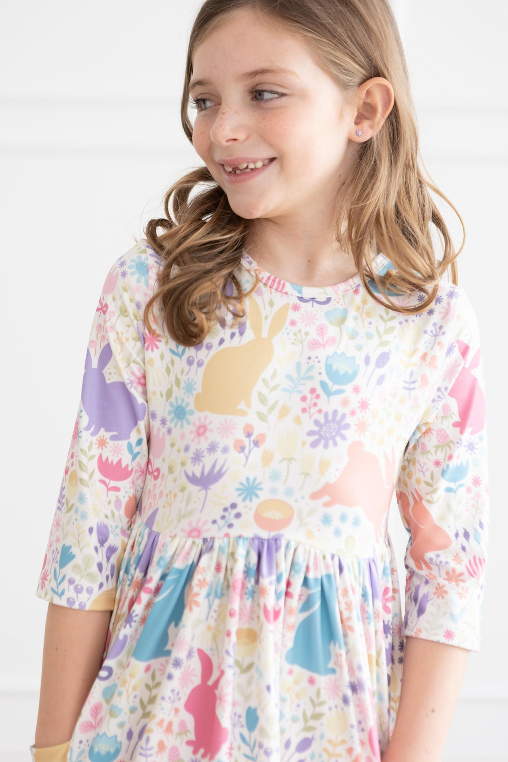 A joyful girl wearing the Pastel Floral Bunnies 3/4 Sleeve Pocket Twirl Dress, showcasing its charming floral design and fun pocket.