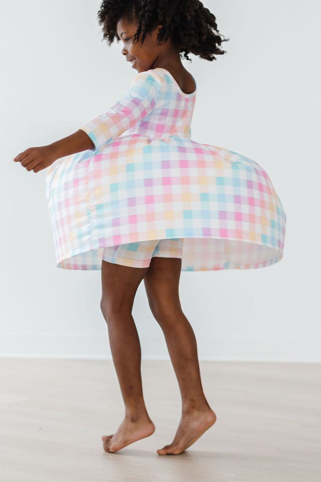 Young girl joyfully twirling in the Pastel Plaid 3/4 Sleeve Pocket Twirl Dress, showcasing its playful skirt and vibrant plaid design, perfect for every dance and adventure.