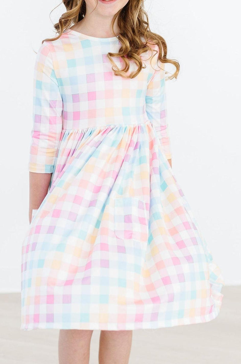 Cheerful young girl wearing the Pastel Plaid 3/4 Sleeve Pocket Twirl Dress, highlighting its stylish scoop back, comfortable fit, and elegant twirl-ready skirt.