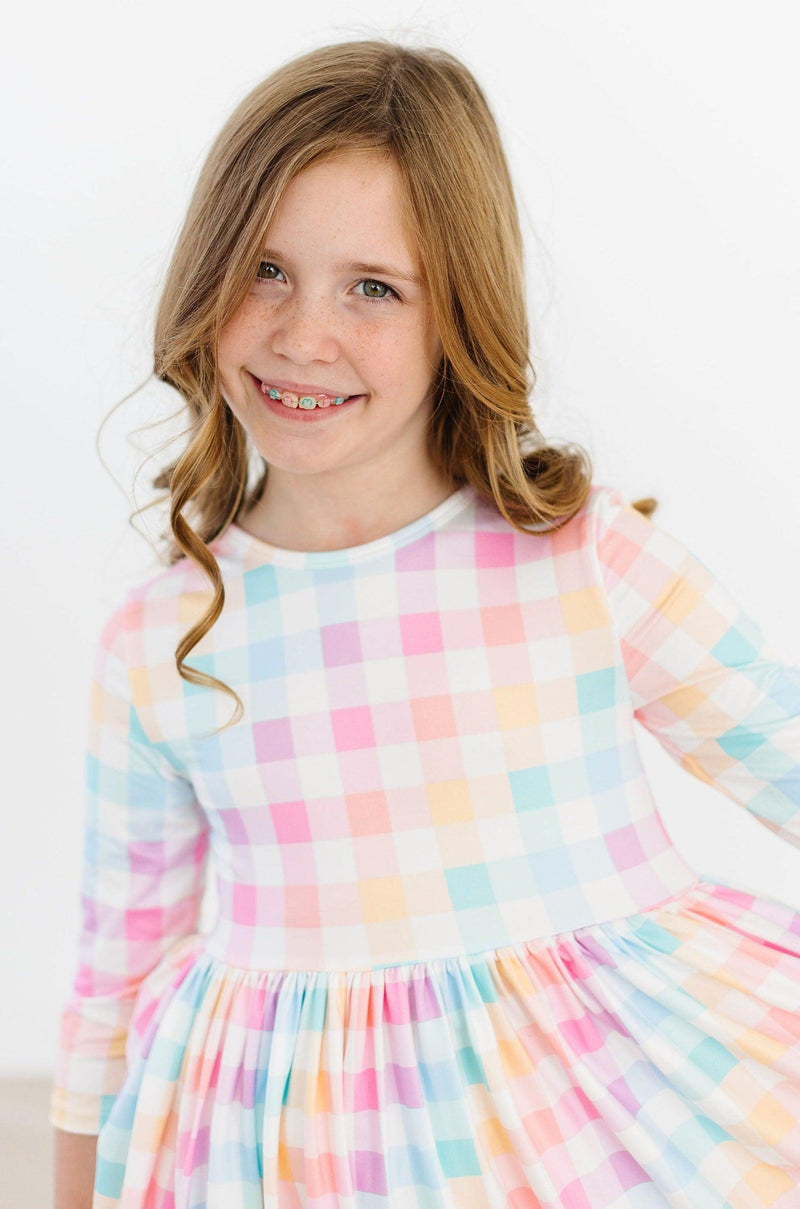 Close-up of a smiling girl wearing a Pastel Plaid 3/4 Sleeve Pocket Twirl Dress by Mila & Rose, highlighting the colorful plaid pattern and comfortable fit.