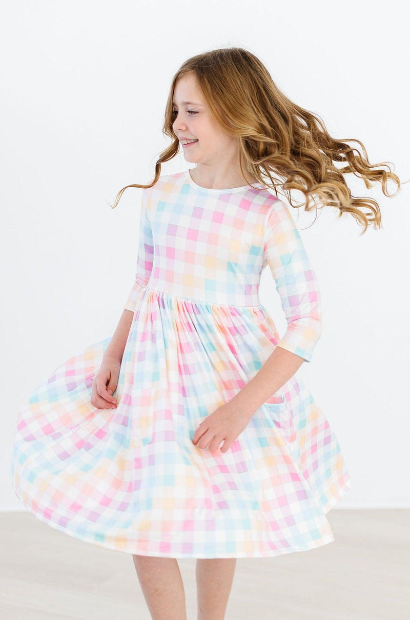 A joyful girl twirling in a Pastel Plaid 3/4 Sleeve Pocket Twirl Dress from Mila & Rose, demonstrating the dress's playful design and full skirt.