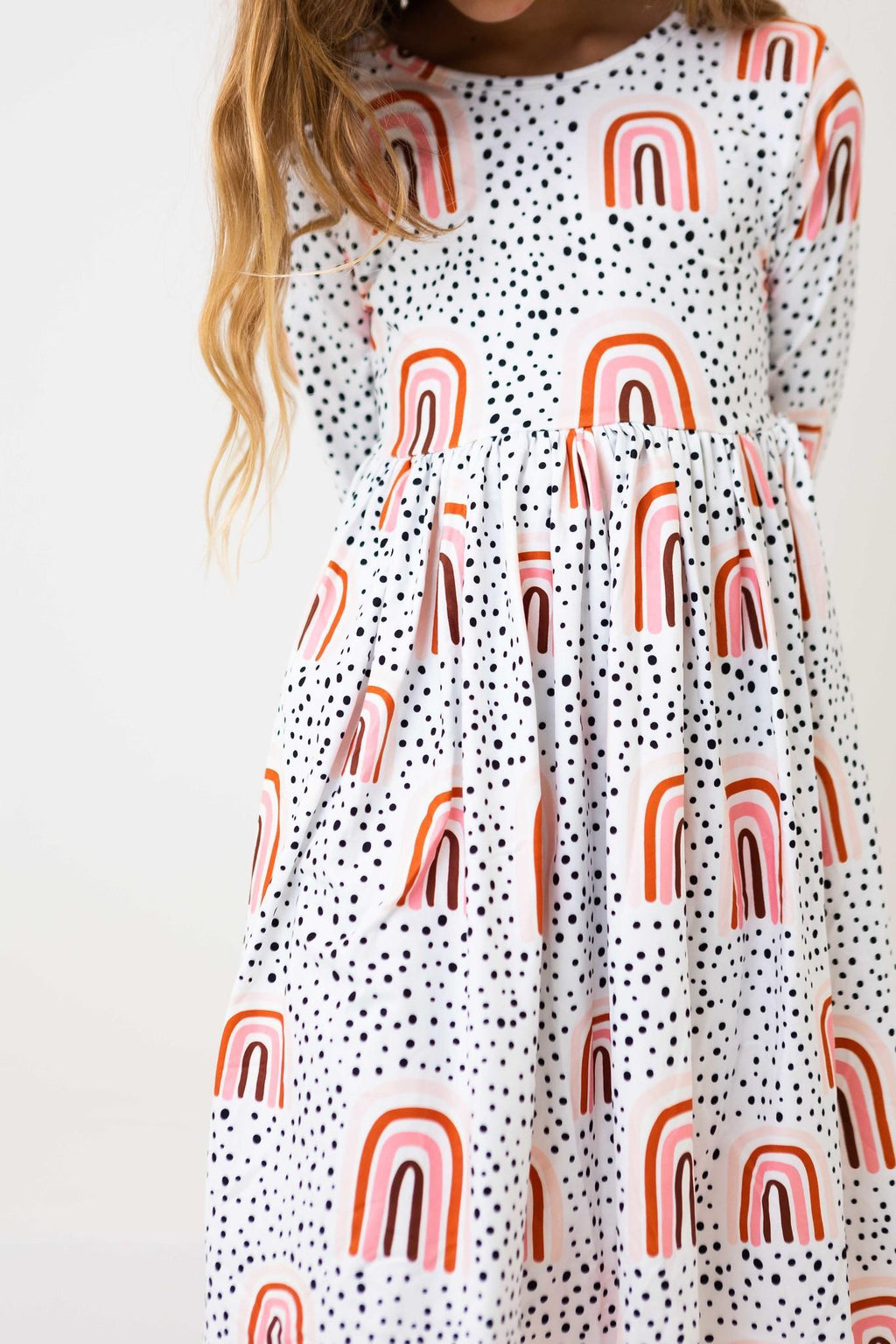 Adorable girl wearing the Peach Rainbow 3/4 Sleeve Pocket Twirl Dress, showcasing a playful design with colorful rainbows and polka dots, perfect for twirling adventures!
