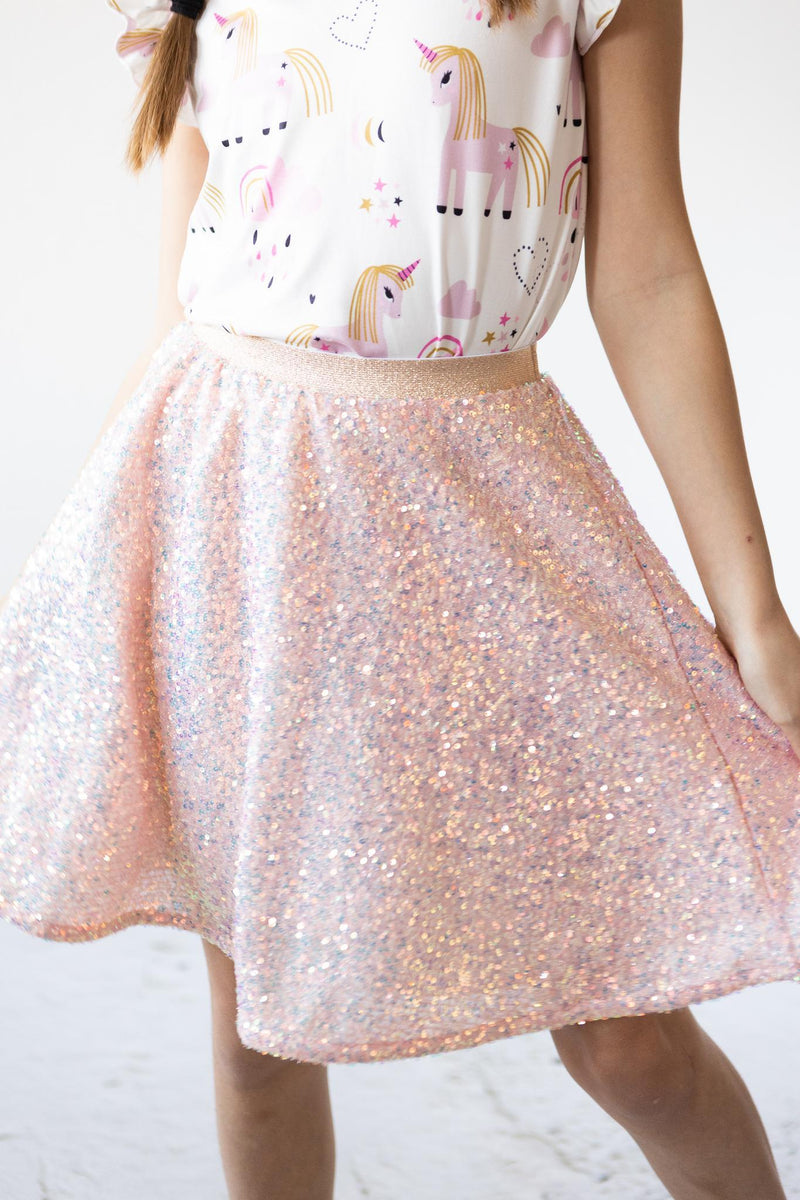 Stylish girl wearing the Peach Sequin Twirl Skort, twirling in a playful pose, showcasing the sparkling sequins against a cute unicorn-themed top.