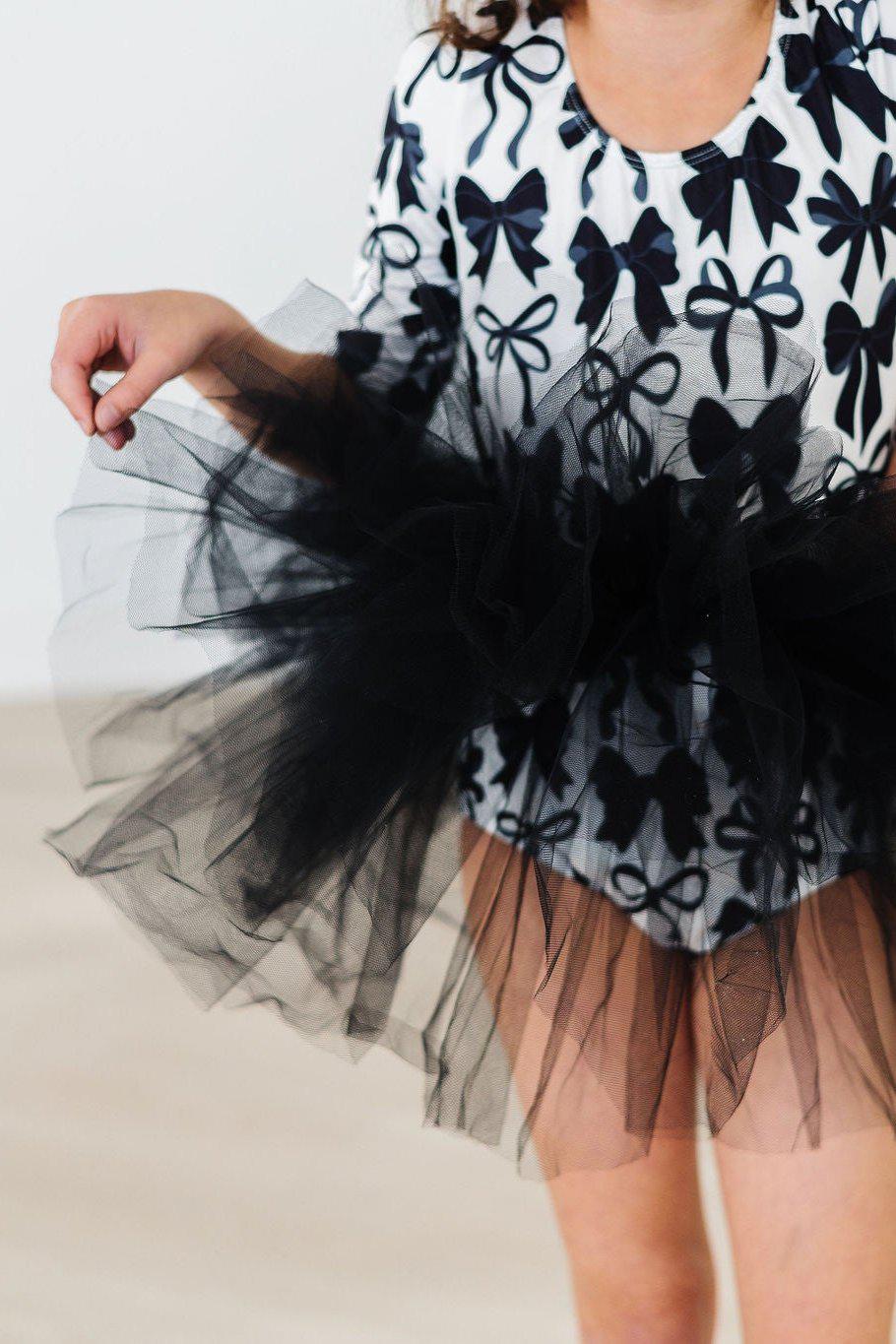 Child wearing the Perfectly Tied 3/4 Sleeve Tutu Leotard, showcasing a playful black tutu with a bow print design, perfect for dance classes.
