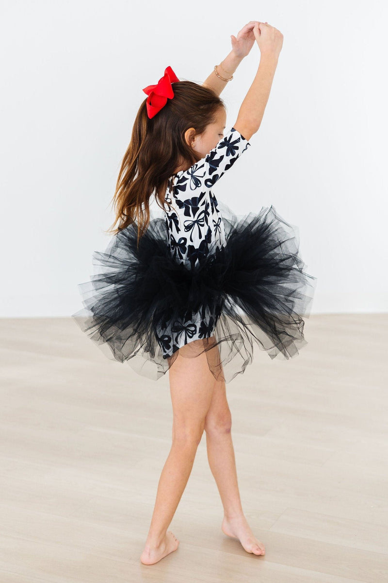 Back view of a girl in the Perfectly Tied 3/4 Sleeve Tutu Leotard with a fluffy black tutu and red bow, captured mid-twirl.