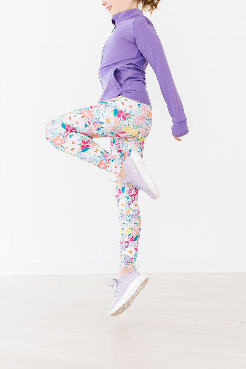 A girl wearing "Petal Power" Girls Active Leggings featuring lively purple flowers, showing off a fun pose while exercising.