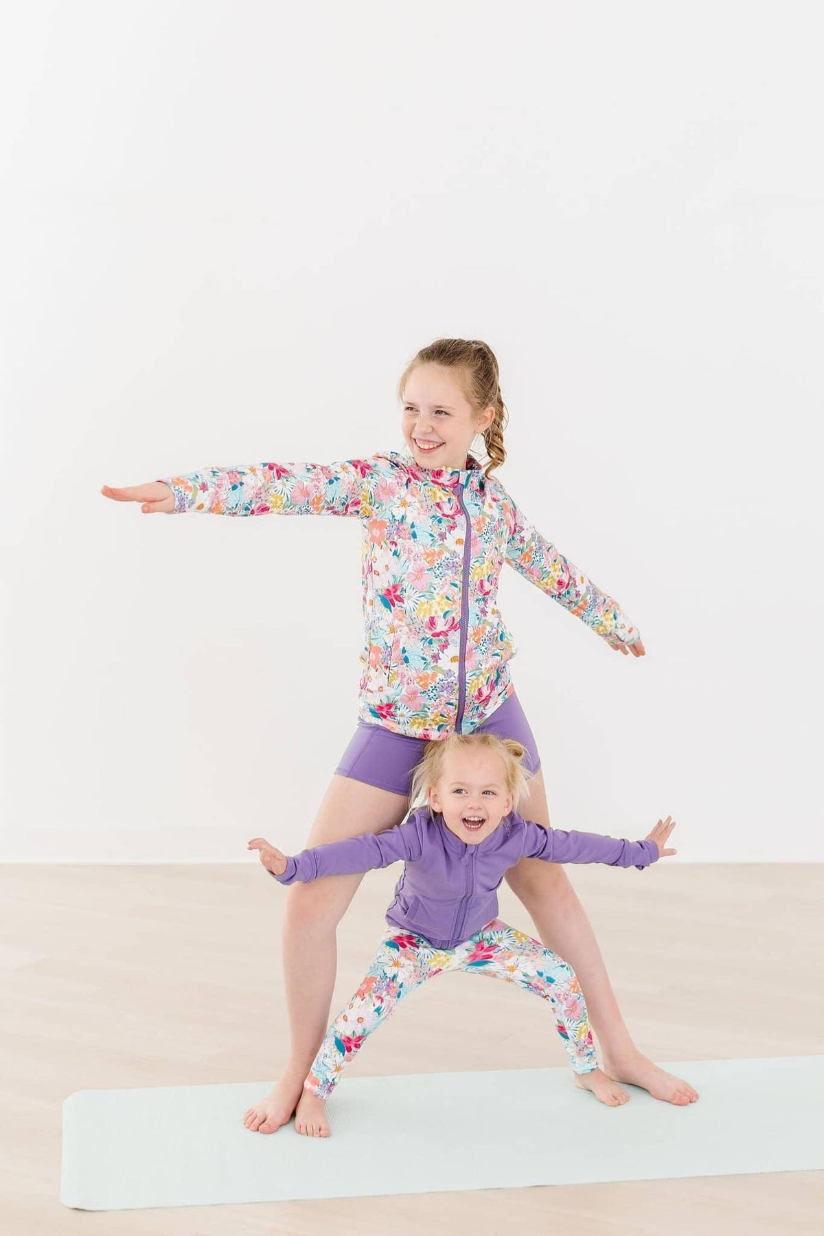 Girls floral active jacket with long sleeves and purple shorts, playful yoga pose indoors