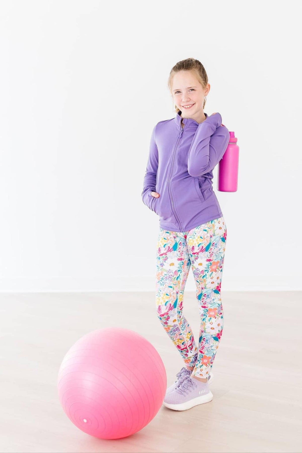 Girls lavender active jacket with zipper, long sleeve, worn with colorful floral leggings and purple sneakers